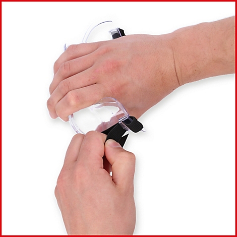 Hände halten eine transparente Schutzbrille mit schwarzem Band und Nadel. Der Arm ist im Hintergrund zu sehen.